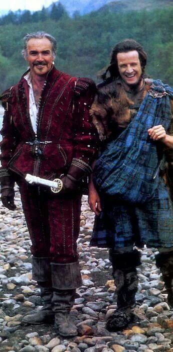 Sean Connery and Christopher Lambert smiling on location whilst filming Highlander. Sean is holding a prop sword.